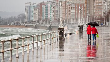 El tiempo hoy 14 de marzo. Dos personas pasean con un paraguas por el paseo mar�timo de Gij�n.