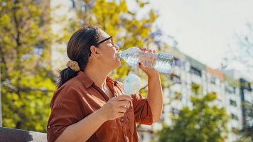 Una mujer bebe agua y se refresca con un ventilador port�til