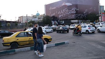 Una mujer y un hombre cruzan el paso peatonal a unos metros de un enorme mural que muestra al presidente estadounidense Donald Trump en un ata�d, acompa�ada de una frase en persa que dice: "mataremos a Trump".