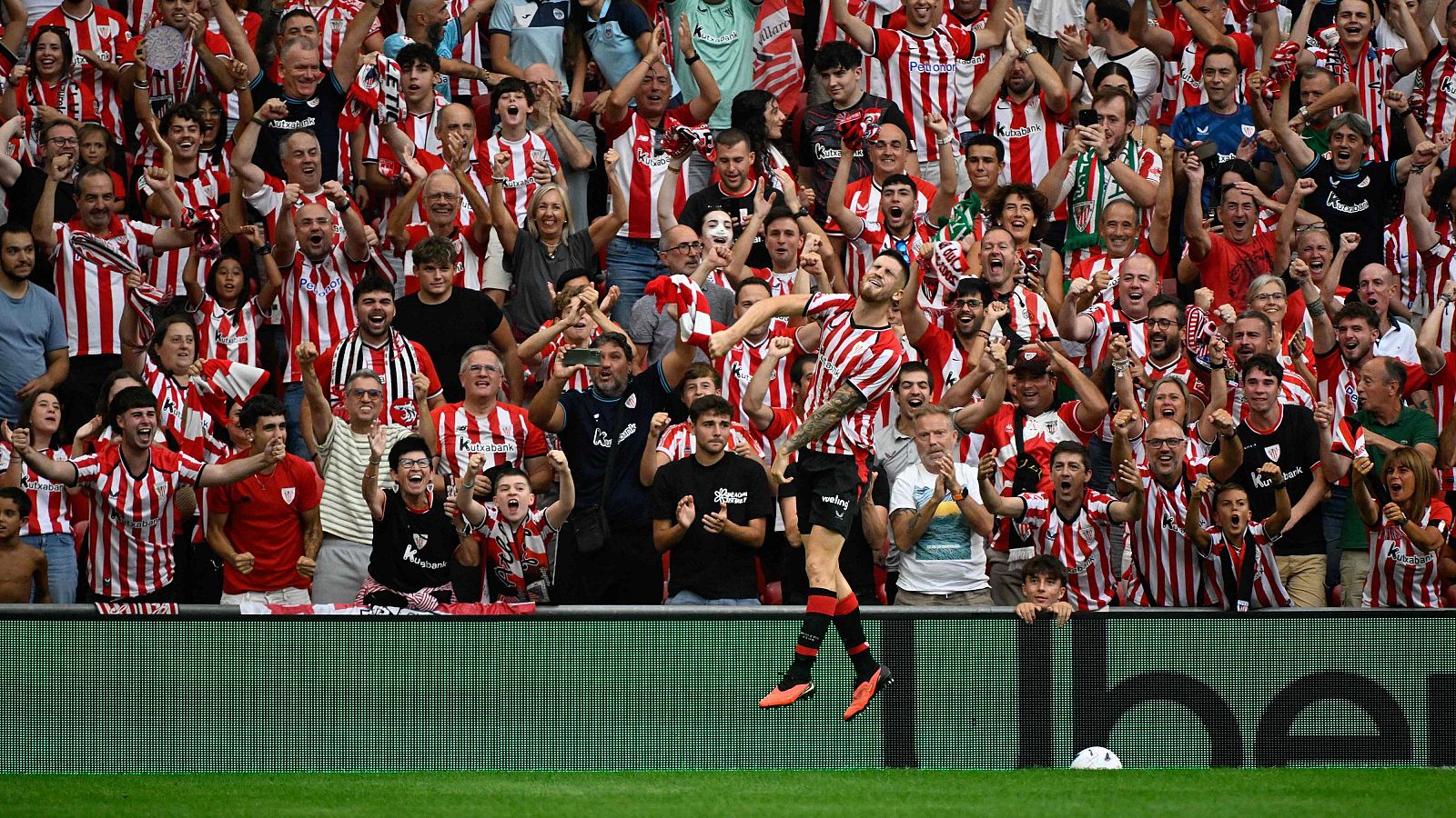 Raúl García (Athletic Club) y Antoine Griezmann (Atlético de Madrid) luchan por el balón en un partido de Primera División. El balón está en el aire, con público al fondo.