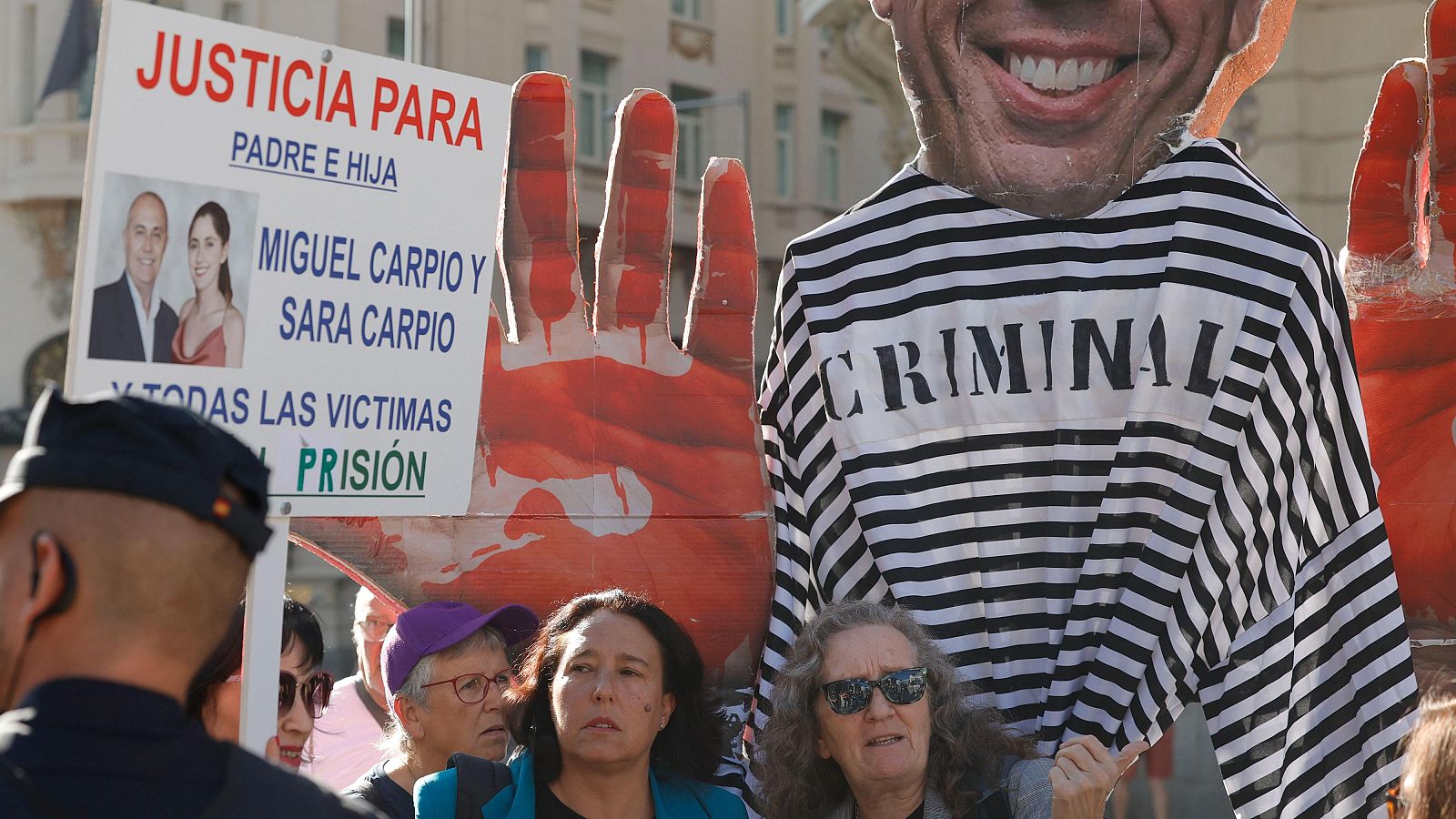 Carlos Mazón, compareciente en el Congreso, con gafas rojas y traje oscuro, sentado ante un micrófono y un dispositivo "AH".