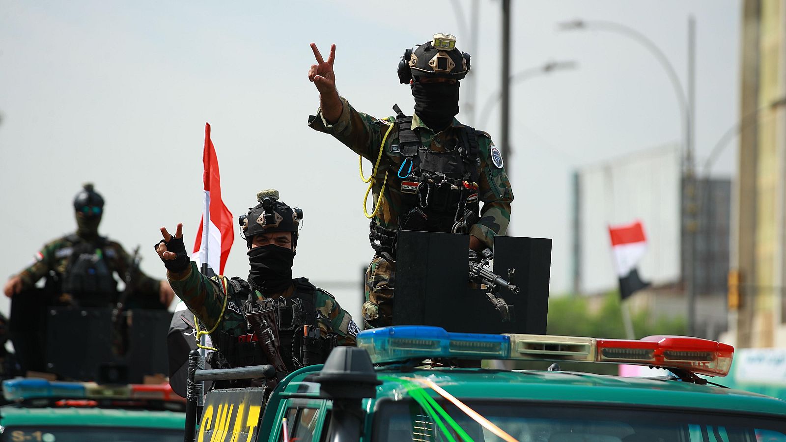 Soldados de las fuerzas especiales iraquíes con pasamontañas celebran a bordo de un vehículo con la palabra "SWAT", haciendo el gesto de la victoria junto a la bandera de Irak.