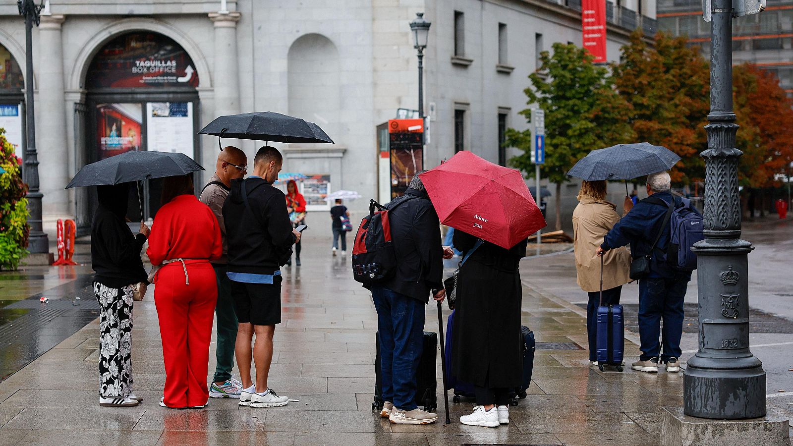 Viandantes se protegen de la lluvia en el centro de Madrid, junto al Teatro Real, este martes