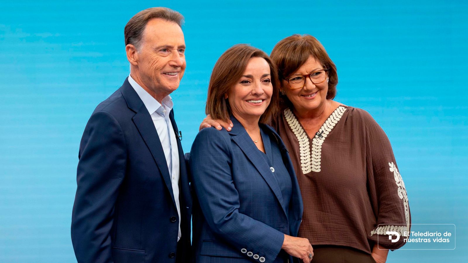 Tres conocidos periodistas y presentadores posan sonrientes en un plató con fondo azul, vistiendo ropa formal y micrófonos de solapa.