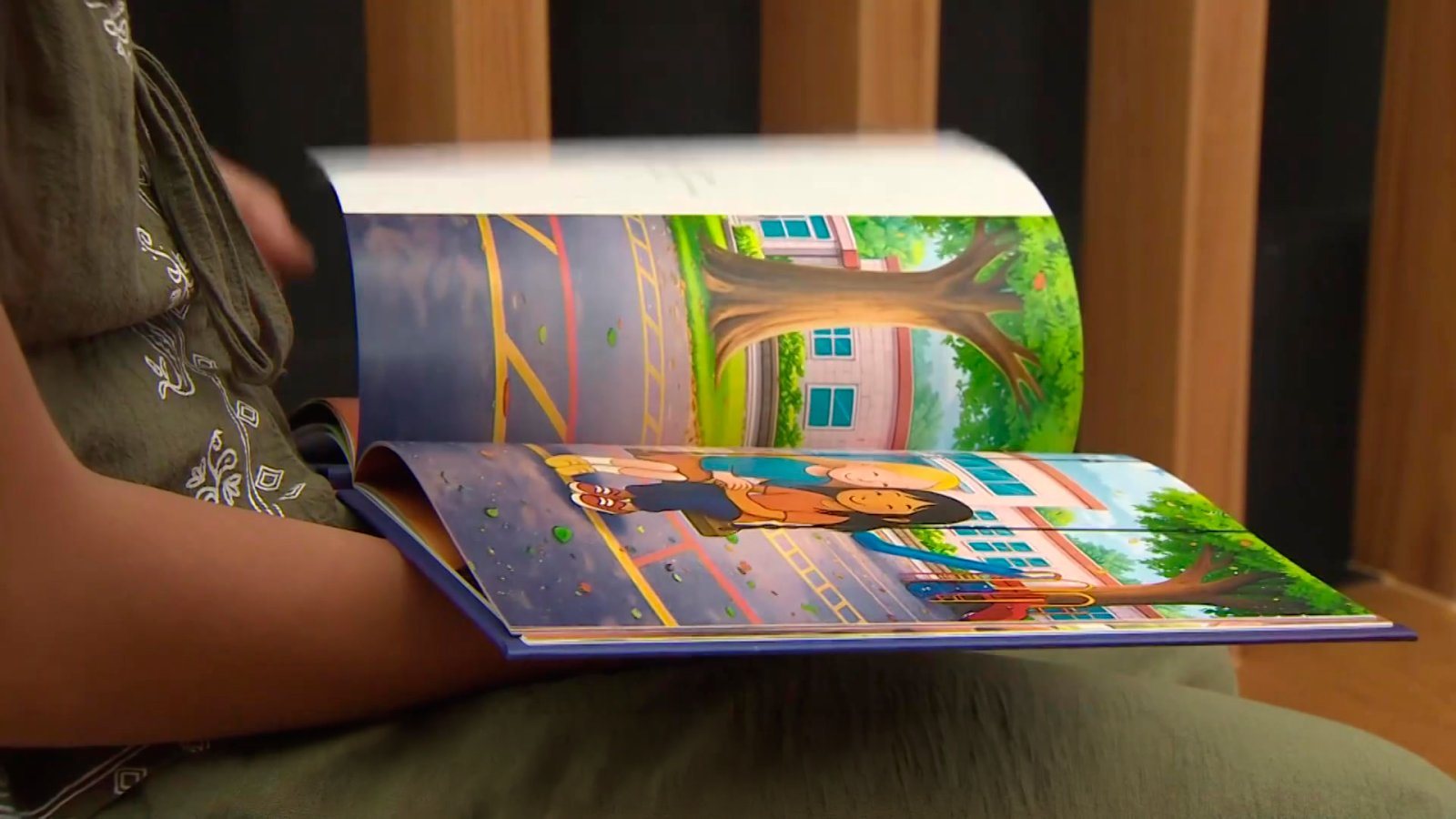 Persona sentada hojea un libro ilustrado con la imagen de dos niños en el patio de un colegio.