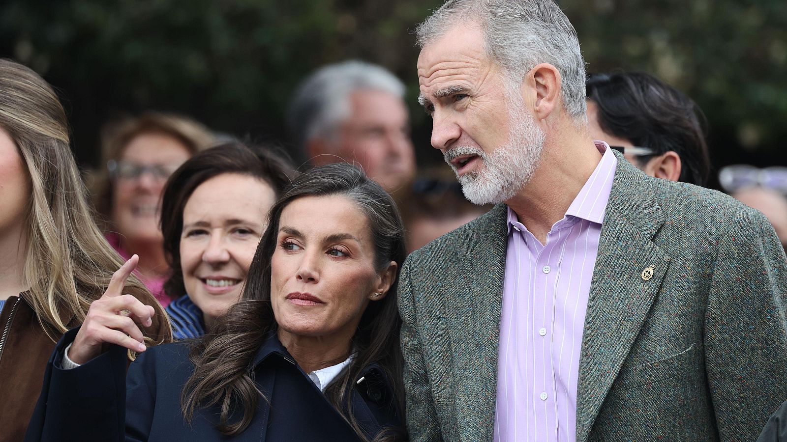 Los reyes Felipe VI y Letizia en un acto al aire libre acompañados de público, con una joven señalando hacia un punto fuera de campo.