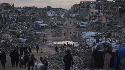 Palestinos caminan junto a edificios destruidos en el norte de la Franja de Gaza, ayer dos de enero.