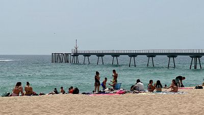 Gent a la platja de Badalona, amb el tram final del Pont del Petroli de fons | ACN: Jordi Pujolar