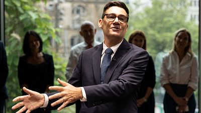 Andy Burnham, Alcalde de Gran Manchester, habla en un evento formal. Viste traje azul marino y gafas, con las manos extendidas en un gesto expresivo. Al fondo, se ve a la audiencia y ventanales. Andy Burnham, Alcalde de Gran Manchester, habla en un evento formal. Viste traje azul marino y gafas, con las manos extendidas en un gesto expresivo. Al fondo, se ve a la audiencia y ventanales.