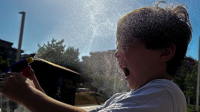 Niño/a de perfil, con el rostro mojado por un pulverizador, sonríe o se sorprende bajo el sol. Gotas de agua brillan en su cabello y cara. Niño/a de perfil, con el rostro mojado por un pulverizador, sonríe o se sorprende bajo el sol. Gotas de agua brillan en su cabello y cara.