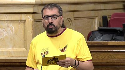 Primer plano de Dani Cornellà, diputado de la CUP, con camiseta amarilla "HI SOM" y logo, sosteniendo tarjeta CUP. Expresión de habla. Primer plano de Dani Cornellà, diputado de la CUP, con camiseta amarilla "HI SOM" y logo, sosteniendo tarjeta CUP. Expresión de habla.