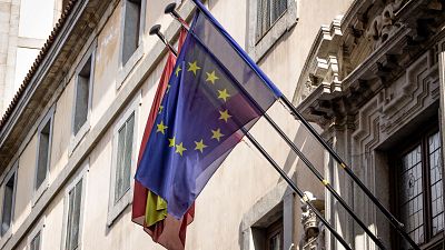 Dos banderas, la de la Unión Europea y la de España, ondean en un balcón de un edificio con arquitectura clásica en Madrid.