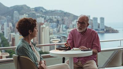 José Sacristán y María Galiana conversan en un balcón con vistas a una ciudad costera, rodeados de una lámpara, un cuaderno y un móvil. José Sacristán y María Galiana conversan en un balcón con vistas a una ciudad costera, rodeados de una lámpara, un cuaderno y un móvil.