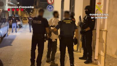 Detención policial en una calle. Dos agentes, Mossos d'Esquadra y Guardia Civil, escoltan a un detenido esposado. Se observan otros agentes y vehículos policiales. Detención policial en una calle. Dos agentes, Mossos d'Esquadra y Guardia Civil, escoltan a un detenido esposado. Se observan otros agentes y vehículos policiales.