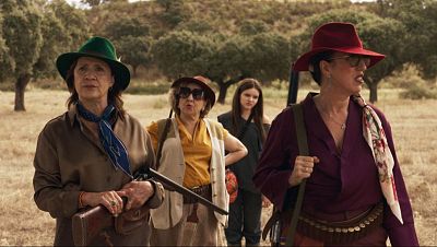 En un fotograma de la película, tres mujeres vestidas con ropa de caza y sombreros se preparan para la jornada, mientras que una cuarta observa. El entorno es rural, con un campo y árboles dispersos, sugiriendo una jornada de caza.