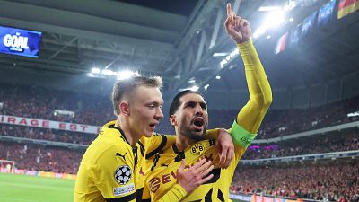 Celebración de gol del Borussia Dortmund en un estadio lleno. Dos jugadores, uno con el brazo en alto, festejan con la afición rival de fondo. Celebración de gol del Borussia Dortmund en un estadio lleno. Dos jugadores, uno con el brazo en alto, festejan con la afición rival de fondo.