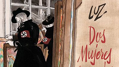 En la portada de un cómic, el título "LUZ Dos Mujeres" destaca en rojo sobre un fondo claro. Dos hombres vestidos de negro, con brazaletes nazis, interactúan con cuadros, mientras que una ventana ofrece una vista exterior. En la portada de un cómic, el título "LUZ Dos Mujeres" destaca en rojo sobre un fondo claro. Dos hombres vestidos de negro, con brazaletes nazis, interactúan con cuadros, mientras que una ventana ofrece una vista exterior.