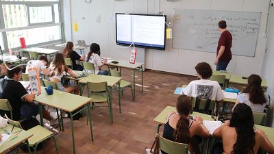 Aula de química con profesor, pizarra con ecuaciones, pantalla interactiva y estudiantes tomando apuntes. Luz natural ilumina el espacio. Aula de química con profesor, pizarra con ecuaciones, pantalla interactiva y estudiantes tomando apuntes. Luz natural ilumina el espacio.