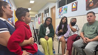 Familia Quintero Boza en la Hermandad Gallega de Venezuela, Caracas, tras sobrevivir a un terremoto en La Guaira. Seis miembros, incluyendo un niño con muletas, sentados en un interior. Familia Quintero Boza en la Hermandad Gallega de Venezuela, Caracas, tras sobrevivir a un terremoto en La Guaira. Seis miembros, incluyendo un niño con muletas, sentados en un interior.