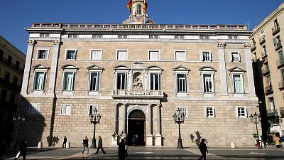 Façana del Palau de la Generalitat de Catalunya amb escultura de Sant Jordi, cúpula amb mosaic i bandera d'Espanya. Plaça amb faroles i vianants. Façana del Palau de la Generalitat de Catalunya amb escultura de Sant Jordi, cúpula amb mosaic i bandera d'Espanya. Plaça amb faroles i vianants.
