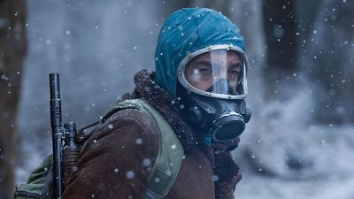 Actor con capucha, máscara antigas y mochila (con arma visible) en escena nevada de bosque. Chaqueta marrón. Actor con capucha, máscara antigas y mochila (con arma visible) en escena nevada de bosque. Chaqueta marrón.