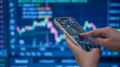 Mano con smartphone dorado muestra gráficos financieros. Fondo con pantalla grande de datos de mercado. Mano con smartphone dorado muestra gráficos financieros. Fondo con pantalla grande de datos de mercado.