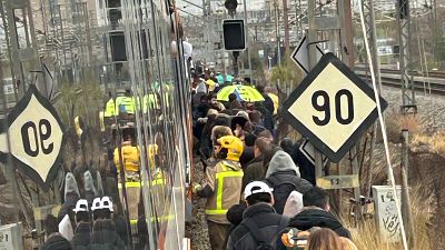 Bomberos ayudan a evacuar a pasajeros de un tren parado.  Multitud de personas bajan del tren, sin indicios de accidente mayor.