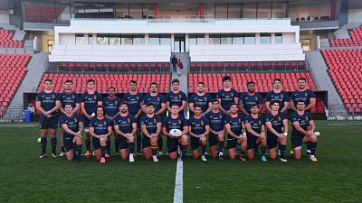 Equipo de rugby español en uniforme azul con detalles amarillo y rojo, posando con un balón. El patrocinador Generali se ve en sus camisetas. Equipo de rugby español en uniforme azul con detalles amarillo y rojo, posando con un balón. El patrocinador Generali se ve en sus camisetas.