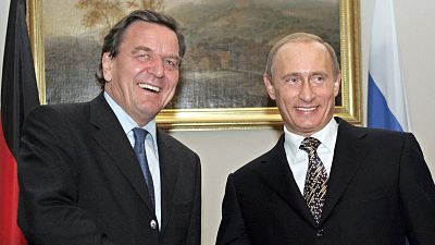 Gerhard Schröder y Vladimir Putin sonríen en un encuentro oficial, con las banderas de Alemania y Rusia al fondo. Gerhard Schröder y Vladimir Putin sonríen en un encuentro oficial, con las banderas de Alemania y Rusia al fondo.