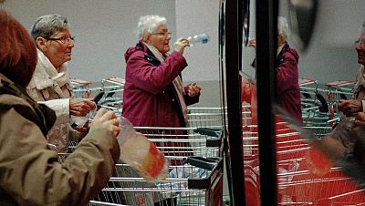 Personas de edad avanzada reciclan envases en una máquina de reciclaje de un supermercado.  Botellas y bolsas de plástico visibles.
