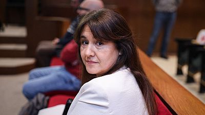 Laura Borràs, en banco rojo, mira hacia atrás.  Fondo con gente y bancos similares. Etiqueta "Borras280325" y "Edició migdia".