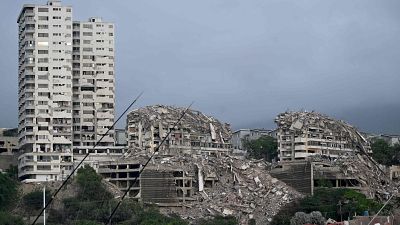 Edificios derrumbados y escombros masivos en una zona urbana bajo un cielo gris, evidenciando la devastación de un desastre natural. Edificios derrumbados y escombros masivos en una zona urbana bajo un cielo gris, evidenciando la devastación de un desastre natural.
