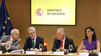 Reunión oficial en el Ministerio de Hacienda con Arcadi España, donde se observan banderas de España y la UE, micrófonos y documentos sobre la mesa. Reunión oficial en el Ministerio de Hacienda con Arcadi España, donde se observan banderas de España y la UE, micrófonos y documentos sobre la mesa.