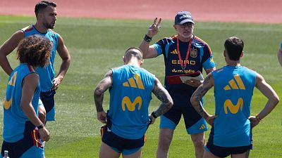 Luis de la Fuente instruye a jugadores de la selección española en un entrenamiento, vistiendo camiseta azul con logos de España, EBIRO y Mapfre, y gorra Adidas.