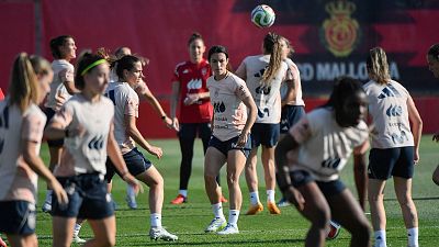 Alexia Putellas, con camiseta de Iberdrola y España, entrena en un campo de césped. Se aprecian logotipos de Adidas y un balón en el aire. Al fondo, el escudo de Palma de Mallorca.