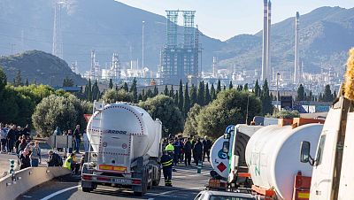 Manifestantes del sector del metal protestan en una carretera murciana, destacando uno con máscara blanca y otro con una camiseta llena de reivindicaciones sindicales. Manifestantes del sector del metal protestan en una carretera murciana, destacando uno con máscara blanca y otro con una camiseta llena de reivindicaciones sindicales.