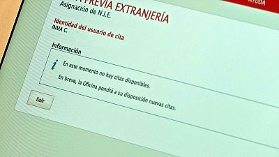Pantalla de ordenador mostrando mensaje de "no hay citas disponibles" para la asignación de N.I.E.  Se indica que habrá nuevas citas próximamente. Botón "Salir".