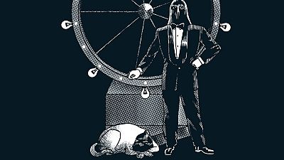 En la portada de un cómic, un personaje enmascarado con esmoquin se apoya en una rueda de la fortuna iluminada, mientras un gato descansa plácidamente.