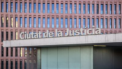 Vista frontal de la Ciutat de la Justícia de Barcelona, amb façana de finestres marrons vermelloses, estructura de formigó gris i el nom del edifici en lletres blanques. Vista frontal de la Ciutat de la Justícia de Barcelona, amb façana de finestres marrons vermelloses, estructura de formigó gris i el nom del edifici en lletres blanques.