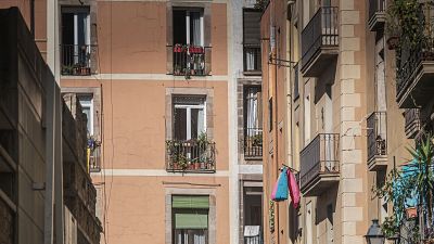 Fachadas de edificios en Barcelona con balcones adornados con plantas y ropa tendida, bajo luz solar directa. Se aprecian detalles arquitectónicos y colores vivos en las prendas. Fachadas de edificios en Barcelona con balcones adornados con plantas y ropa tendida, bajo luz solar directa. Se aprecian detalles arquitectónicos y colores vivos en las prendas.