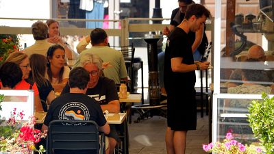 Terraza de restaurante con clientes sentados en mesas, un camarero toma nota y plantas decorativas. Ambiente relajado. Terraza de restaurante con clientes sentados en mesas, un camarero toma nota y plantas decorativas. Ambiente relajado.