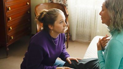 Olivia Delcán y Emma Suárez comparten un momento íntimo en una habitación luminosa. Olivia, de rubio y sudadera morada, se arrodilla ante Emma, de pelo canoso y jersey azul turquesa. Olivia Delcán y Emma Suárez comparten un momento íntimo en una habitación luminosa. Olivia, de rubio y sudadera morada, se arrodilla ante Emma, de pelo canoso y jersey azul turquesa.