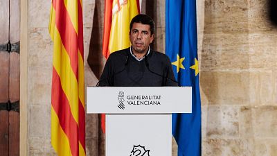 El presidente de la Generalitat Valenciana, Carlos Mazón, habla en un atril con las banderas de la Comunidad Valenciana, España y la UE detrás.