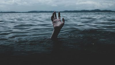 Mano emergiendo de agua oscura y con dedos extendidos; cielo nublado y fondo montañoso. Atmósfera sombría. Mano emergiendo de agua oscura y con dedos extendidos; cielo nublado y fondo montañoso. Atmósfera sombría.