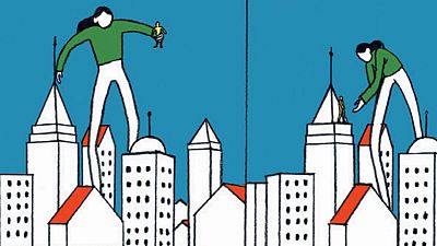 Dos viñetas de un cómic muestran a una figura femenina de gran tamaño interactuando con figuras humanas diminutas en un entorno urbano con edificios blancos y tejados rojos, bajo un cielo azul. Dos viñetas de un cómic muestran a una figura femenina de gran tamaño interactuando con figuras humanas diminutas en un entorno urbano con edificios blancos y tejados rojos, bajo un cielo azul.