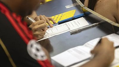 Manos d'un estudiant omplint un formulari de les PAU 2026 amb un bolígraf blanc, sobre una taula fosca amb bolígrafs addicionals i una carpeta groga texturitzada. Manos d'un estudiant omplint un formulari de les PAU 2026 amb un bolígraf blanc, sobre una taula fosca amb bolígrafs addicionals i una carpeta groga texturitzada.