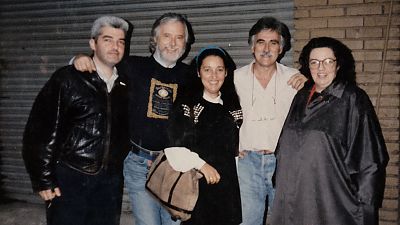 Grupo de cinco personas (cuatro hombres y una mujer) posando informalmente, con vestimenta casual y expresiones amigables, frente a una puerta enrollable metálica. Grupo de cinco personas (cuatro hombres y una mujer) posando informalmente, con vestimenta casual y expresiones amigables, frente a una puerta enrollable metálica.