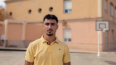Mohamed Esqueta Albert, con polo amarillo y micrófono, posa en una cancha deportiva con un edificio y aro de baloncesto al fondo. Mohamed Esqueta Albert, con polo amarillo y micrófono, posa en una cancha deportiva con un edificio y aro de baloncesto al fondo.
