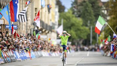 Ciclista con maillot verde lima cruzando la meta, quitándose el casco tras una carrera, rodeado de público que lo celebra. Ciclista con maillot verde lima cruzando la meta, quitándose el casco tras una carrera, rodeado de público que lo celebra.