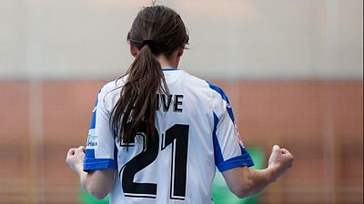 Una jugadora de fútbol sala, con el pelo recogido en una coleta, celebra un gol con los puños cerrados. Lleva una camiseta deportiva blanca con detalles azules y el nombre y número del dorsal visibles en la espalda. Una jugadora de fútbol sala, con el pelo recogido en una coleta, celebra un gol con los puños cerrados. Lleva una camiseta deportiva blanca con detalles azules y el nombre y número del dorsal visibles en la espalda.